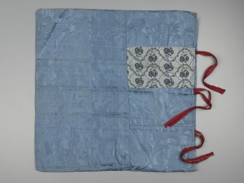 Een sloop van blauwe damast met blauwe bloemmotieven, sluiting bestaat uit rode bandjes