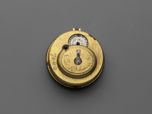 Horloge met witgeëmailleerde wijzerplaat, waarin een liggende vrouw met een bazuin.