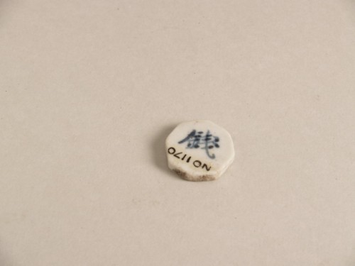 Miniatuurtegel, achthoekig, wit geglazuurd met blauw decor van Chinese karakters in reliëf